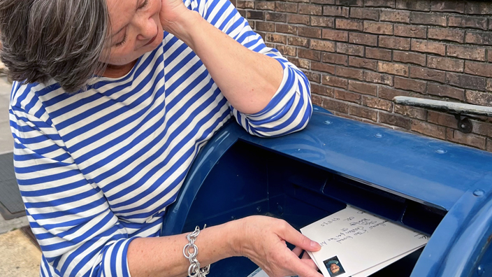 A woman places a stamped envelope inside a blue collection box