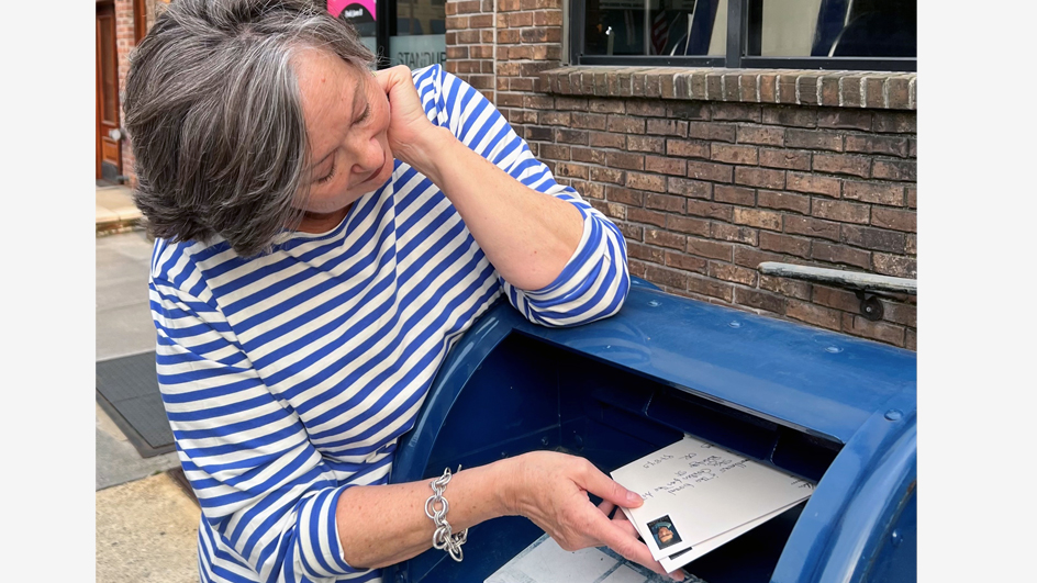 A woman places a stamped envelope inside a blue collection box