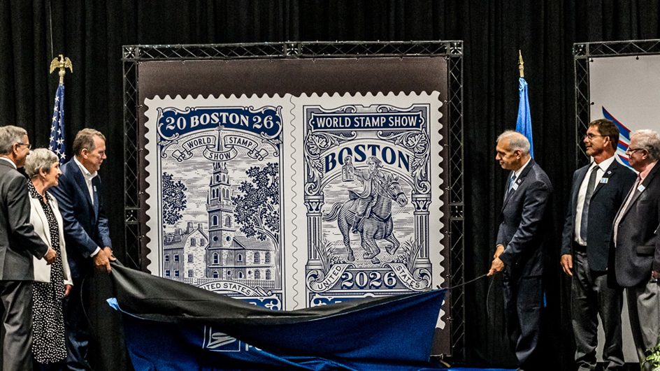 People stand on a stage in a darkened auditorium and watch as a man in a suit and tie pulls away a curtain covering two large posters displaying vintage-style stamp images