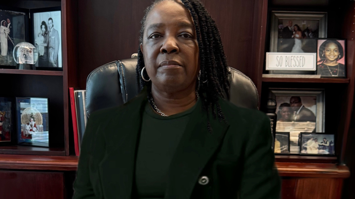 A woman wearing a business suit sits at a desk in an office