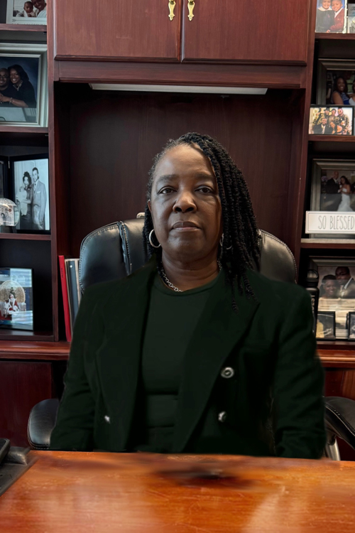 A woman wearing a business suit sits at a desk in an office