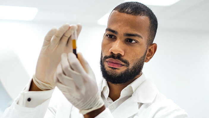 A man wearing a lab coat examines a vial of blood