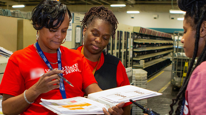 A group of people gather together on the workroom floor of a postal processing plant