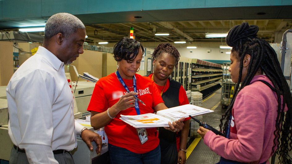 A group of people gather together on the workroom floor of a postal processing plant