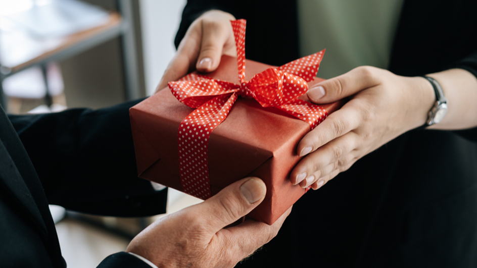 Two sets of hands exchange a gift-wrapped box