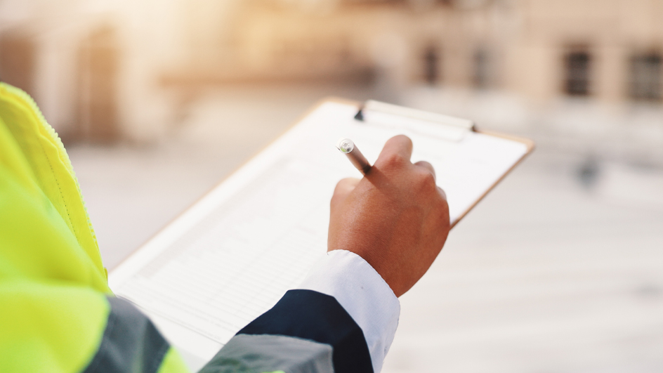 A man who wears a reflective safety vest and whose face is not seeing wields a clipboard