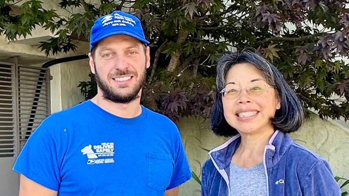 A man in a blue Postal Service T-shirt stands next to a smiling woman
