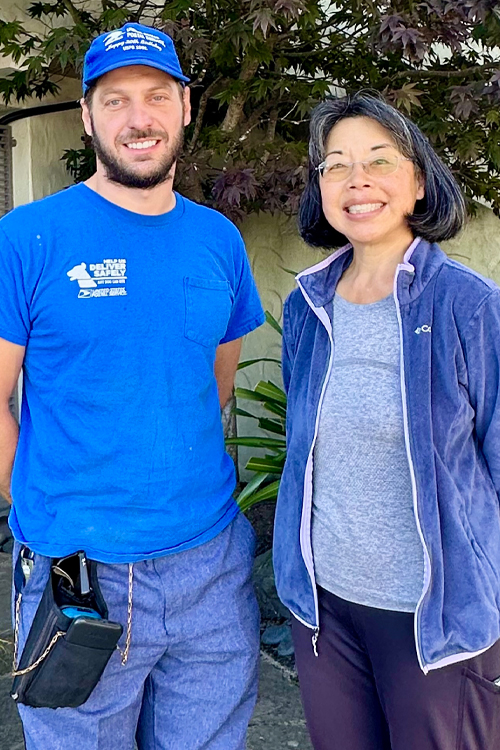 A man in a blue Postal Service T-shirt stands next to a smiling woman