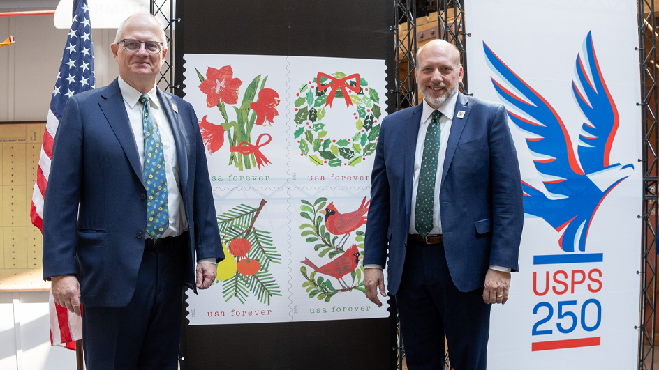 Two men in suits stand next to a postage stamp poster.