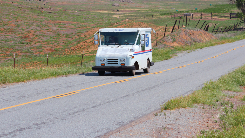 A postal delivery vehicle travels along a road