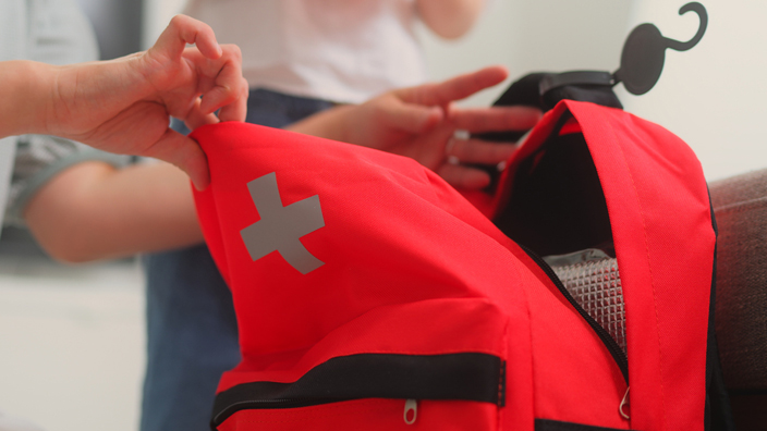 A woman opens a red duffel bag bearing an emergency logo as a small child watches