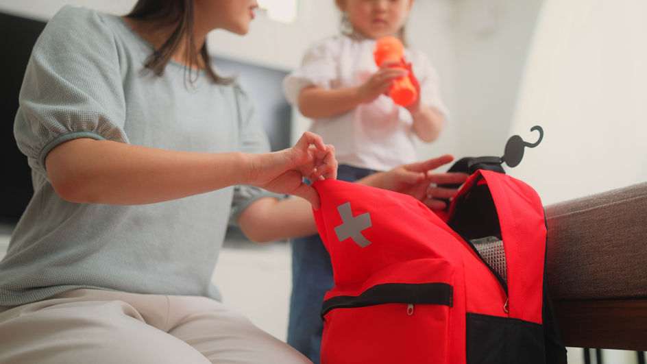A woman opens a red duffel bag bearing an emergency logo as a small child watches