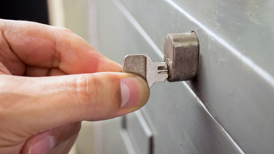 A man’s hand is shown turning a key in a file cabinet lock
