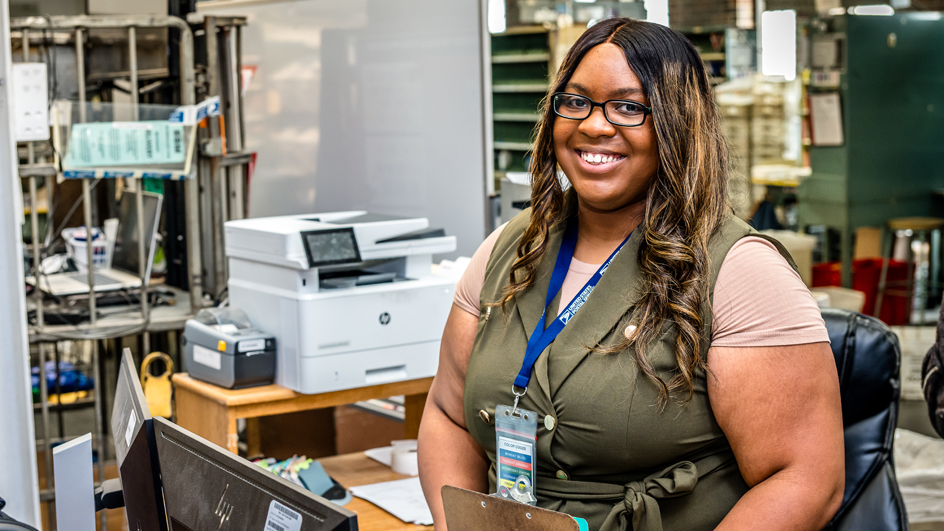 A smiling woman stands near a retail counter in a Post Office