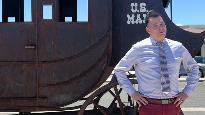 A man stands in front of a vintage mail wagon