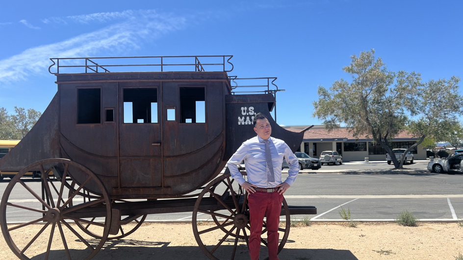 A man stands in front of a vintage mail wagon