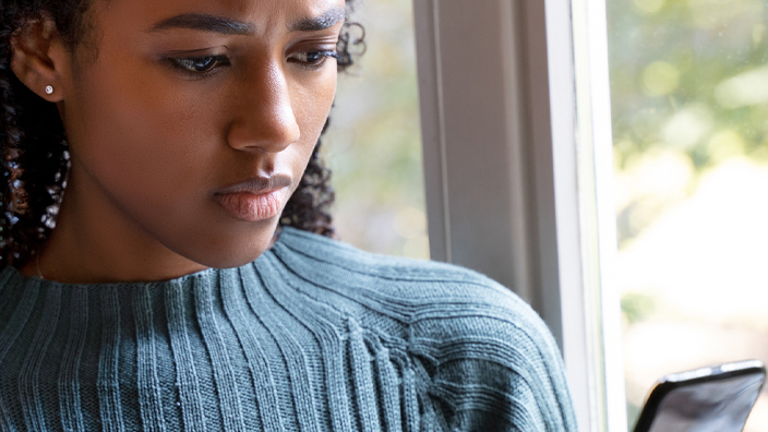 A woman with a skeptical expression looks at her smartphone