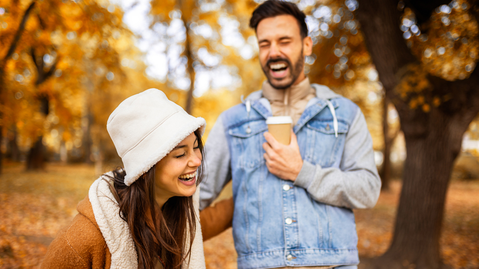 A couple laughs while walking through a wooded area during autumn