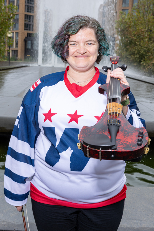 A woman wearing a hockey jersey holds a fiddle