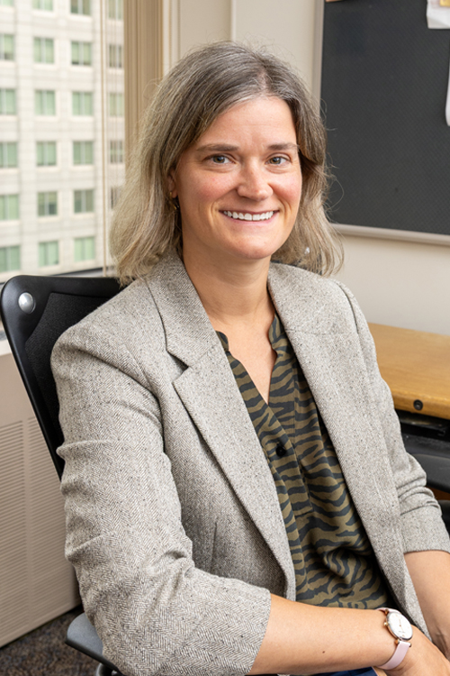 A woman wearing a business suit sits at a desk in an office