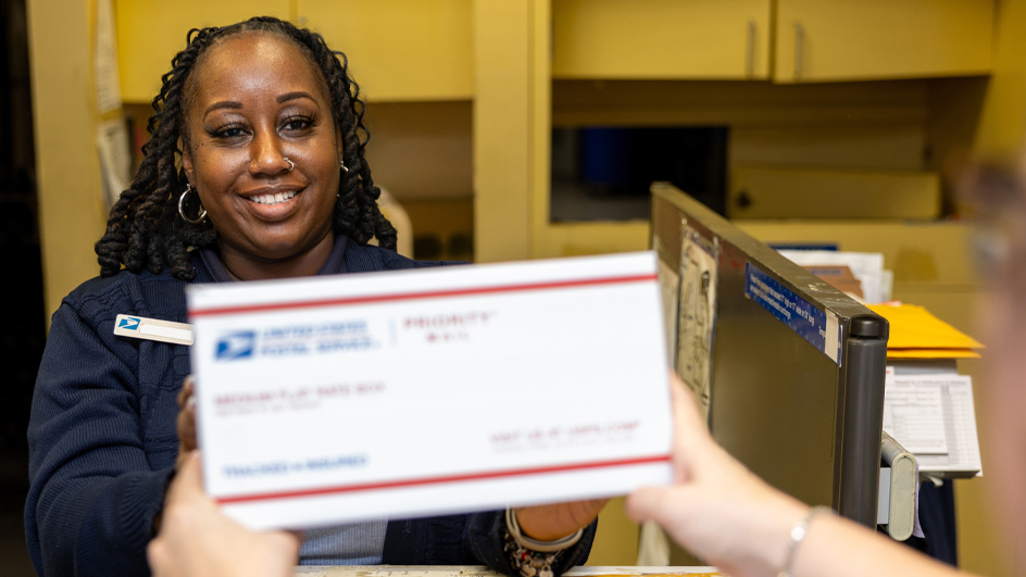 A customer passes a Priority Mail package to a USPS retail associate
