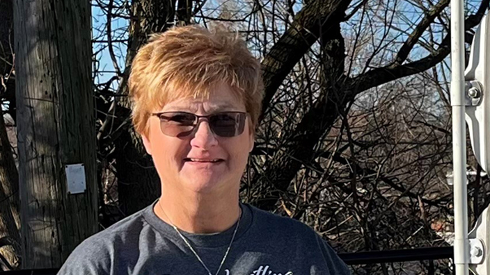A smiling woman stands next to a Postal Service delivery vehicle