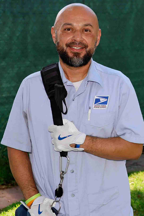 A man wearing a postal uniform smiles