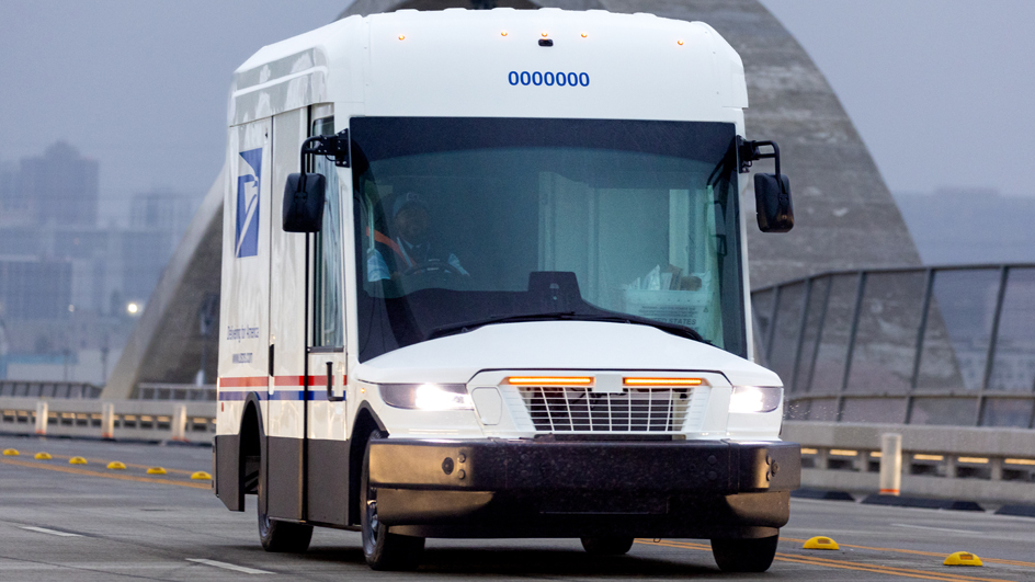 A next-generation Postal Service delivery vehicle driving across a bridge.