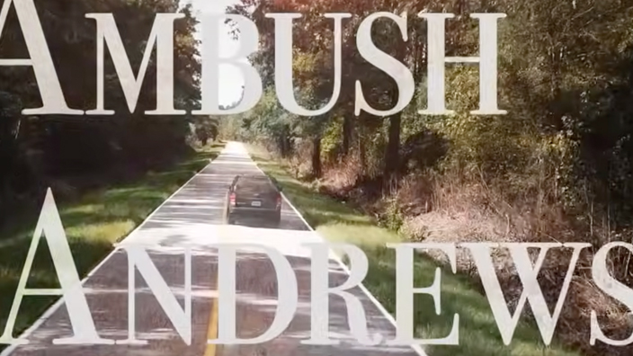 A screenshot from a documentary that shows the title “Ambush in Andrews” over a scene of a car traveling along a tree-lined rural road