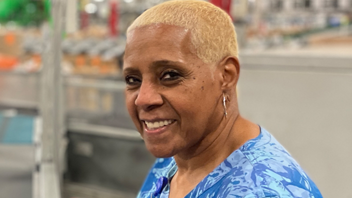 A smiling woman sits at a package sorting machine inside a postal processing plant