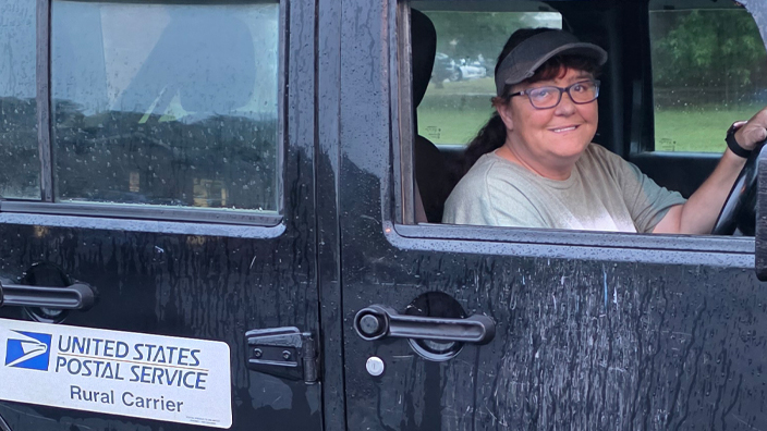 A woman sits in a Jeep with a Postal Service decal on a rear passenger door