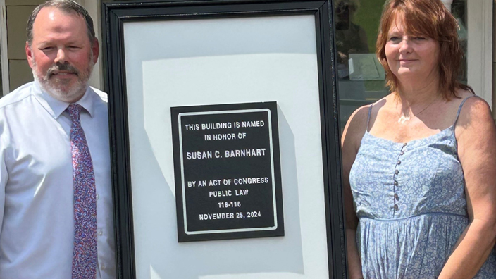 People stand next to a plaque outside a Post Office building