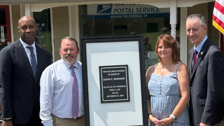 People stand next to a plaque outside a Post Office building
