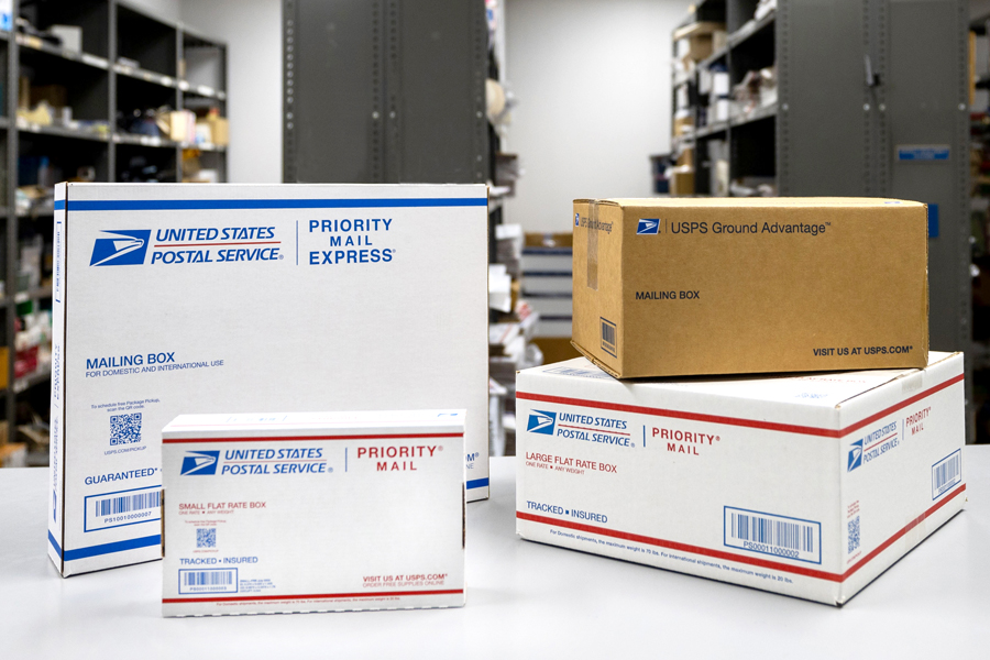 An array of USPS-branded shipping boxes displayed on a table in a Post Office workroom