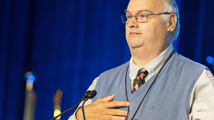 A man stands at a lectern and speaks