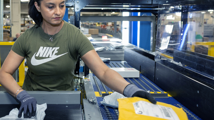 A woman operates a package sorting machine inside a postal processing facility