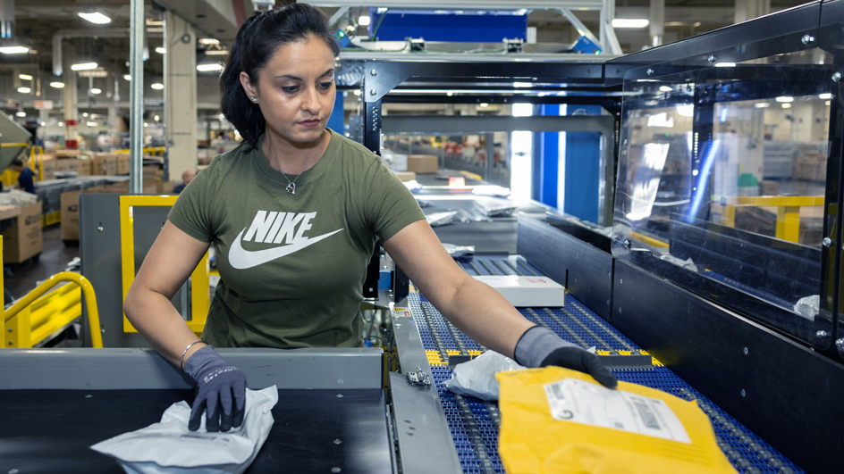A woman operates a package sorting machine inside a postal processing facility