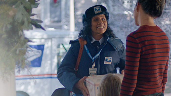 A graphic that shows a smiling USPS mail carrier standing on the snowy front stoop of a residential home next to the words “Delivering Since 1775”