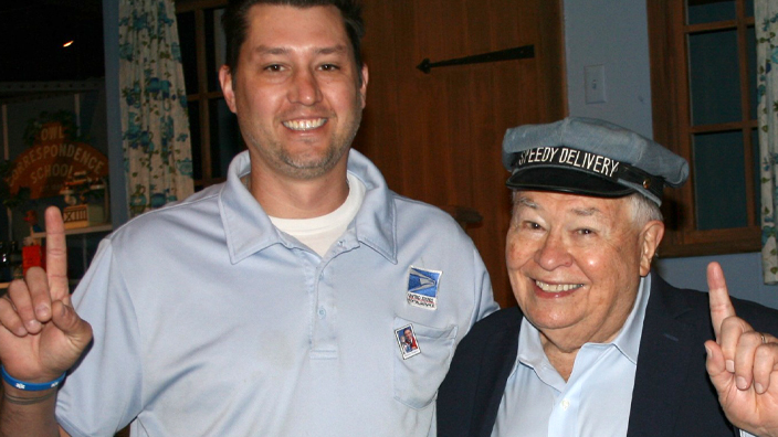 A man in a postal uniform stands next to an older man