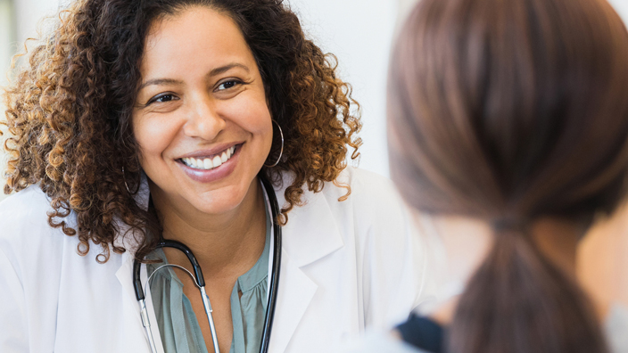 A female doctor sits at a desk and speaks to an unseen patient