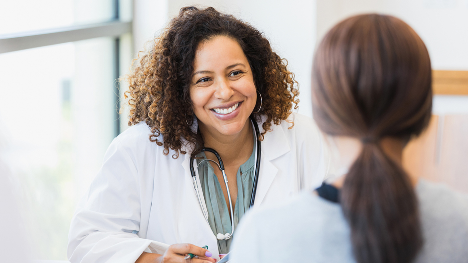 A female doctor sits at a desk and speaks to an unseen patient