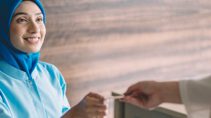 A hand is shown tapping a credit card on a handheld reader in a medical office