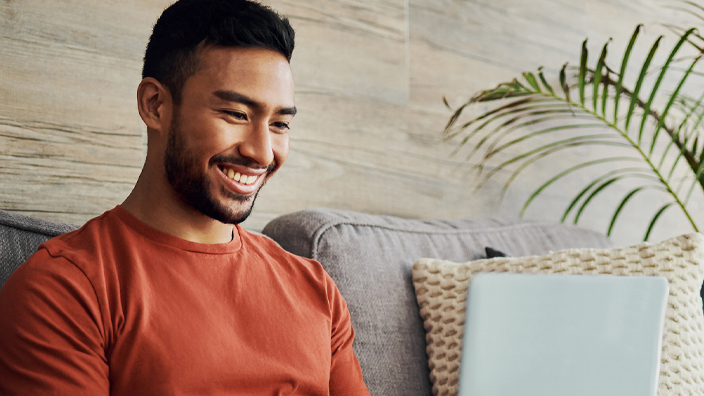 A man sits on his sofa looking at a laptop
