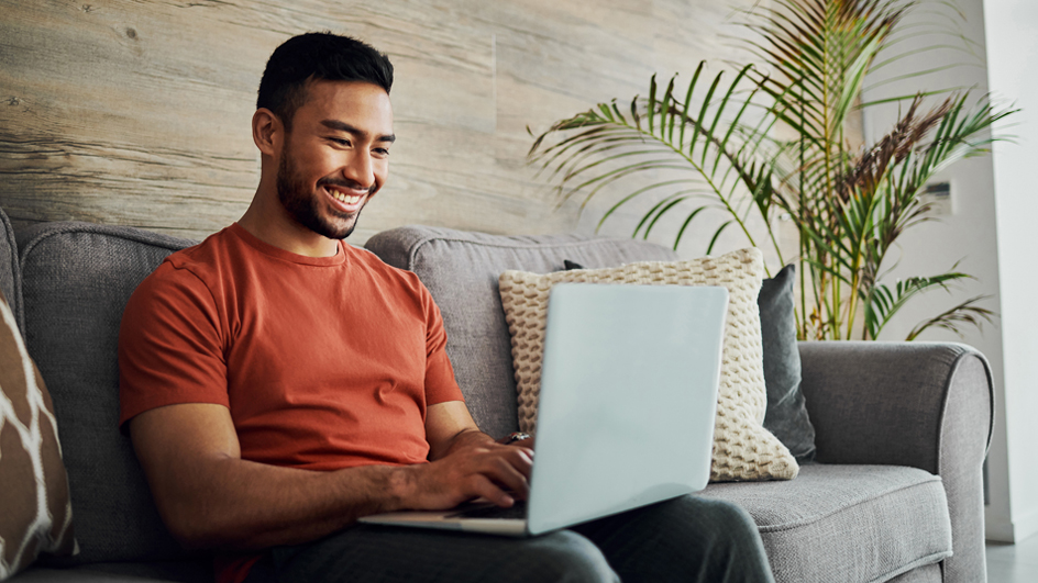 A man sits on his sofa looking at a laptop