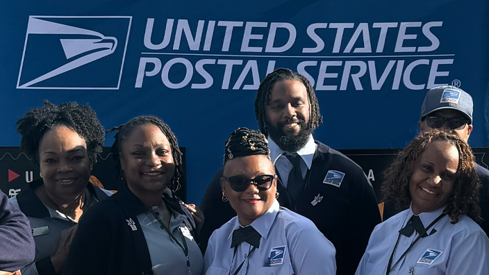 A group of uniformed postal employees smiling on the White House lawn