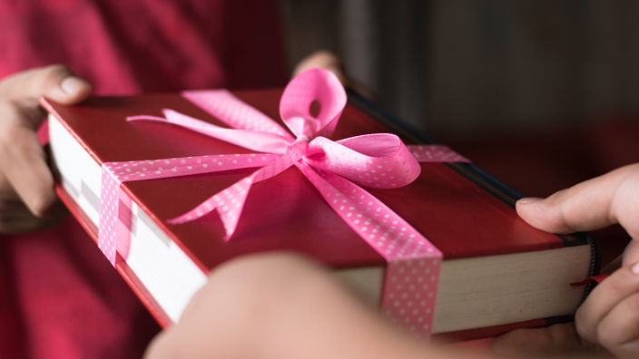 A person receives a gift of a book decorated with a pink bow.
