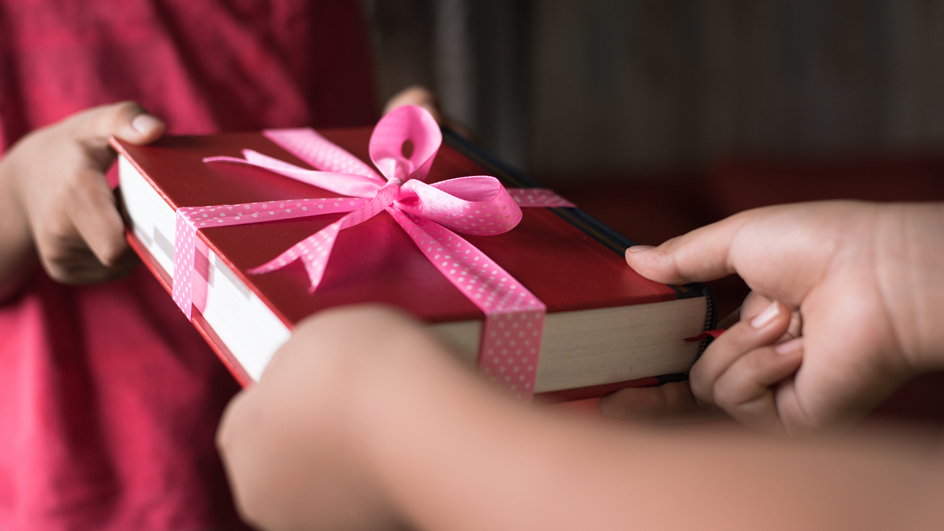 A person receives a gift of a book decorated with a pink bow.