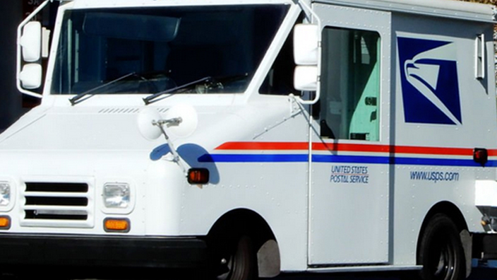 A USPS delivery vehicle parked next to a gas station pump