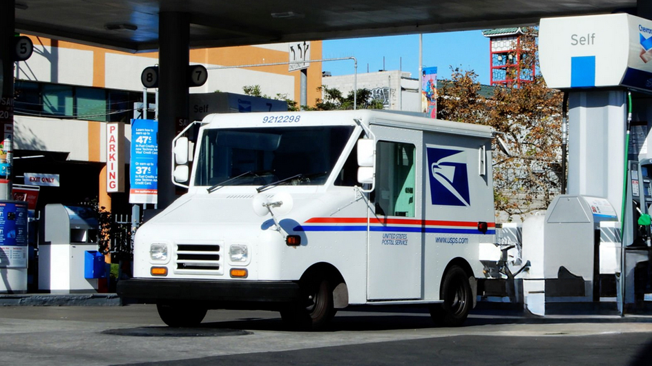 A USPS delivery vehicle parked next to a gas station pump