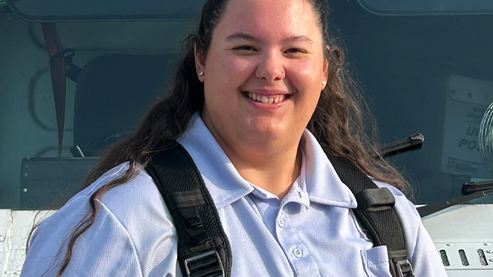 A woman in a postal uniform smiles while standing near a USPS delivery vehicle